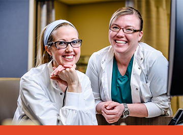 two female medical staff members smiling at a workstation